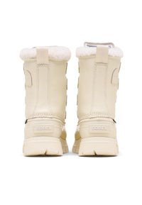 Bottes imperméables beige clair avec un col en fausse fourrure, une tige en cuir texturé et une semelle épaisse et robuste ; elles présentent le logo Sorel à l'arrière.
