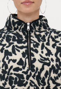 Pulover iz flisa z visokim ovratnikom, z vzorcem črno-kremskega leoparda, z zadrgo in mehkim teksturiranim materialom.
