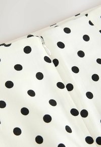 Tissu blanc à pois noirs espacés régulièrement, avec une fermeture éclair blanche le long d'une couture.