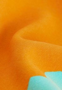 Tessuto di cotone arancione con una texture liscia, caratterizzato da un ampio motivo a blocchi turchesi. Il tessuto ha una finitura opaca e una leggera morbidezza.