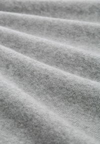 Tissu gris clair avec une texture douce, présentant des plis délicats et une surface lisse et uniforme. Le matériau semble chaud et légèrement fin.