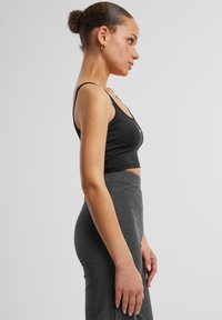 Black cropped tank top with thin straps, featuring a fitted design. Paired with high-waisted, textured gray ribbed leggings.