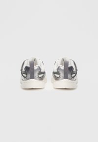 Γκρι και λευκά αθλητικά παπούτσια με υφασμάτινο σχεδιασμό, που διαθέτουν επενδεδυμένους γιακάδες, ταινία έλξης και αντίθετες μαύρες λεπτομέρειες στα πλάγια.