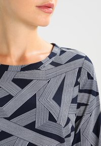 Maglietta navy con un motivo geometrico di linee bianche di diversa larghezza, scollatura rotonda e una trama di tessuto morbida.