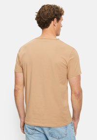Beige Kurzarm-T-Shirt mit engem Rundhalsausschnitt, aus glattem Stoff gefertigt, das ein einfaches, schmuckloses Design aufweist.