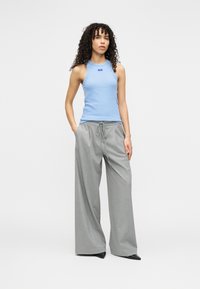 Ανοιχτό μπλε αμάνικο τοπ και γκρι παντελόνι φαρδύ με κορδόνι στη μέση· λείες υφές και άνετη εφαρμογή, με λεπτομέρεια μικρού λογότυπου.