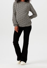 Maglietta a maniche lunghe nera e crema con un motivo a foglia, abbinata a pantaloni neri e sneaker bianche. Tessuto liscio con una vestibilità comoda.