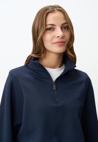 Pullover navy a mezze zip in tessuto liscio, con colletto alto e zip elegante, maniche lunghe e vestibilità comoda.