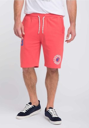 Shorts de couleur corail en tissu doux, avec une taille élastique à cordon, des poches latérales et un imprimé graphique avec du texte sur la jambe gauche.