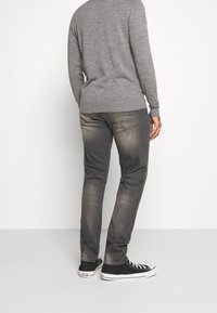 Suéter gris, jeans gris oscuro con un lavado desgastado y zapatillas negras con suelas blancas. El conjunto presenta un ajuste casual y texturas suaves.