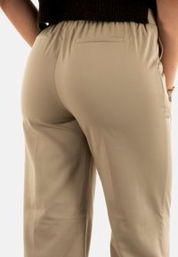Pantaloni leggeri beige con vita elastica, dotati di due tasche posteriori e una texture liscia, mostrati da dietro.