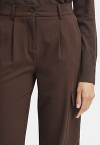Hnědé formální kalhoty s přehyby, předními kapsami a boční kapsou. Obsahují zapínání na jeden knoflík a texturovanou látku.