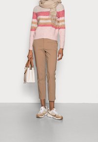 Gebreide trui met roze en beige strepen, beige cropped broek, witte en beige sneakers, en een crèmekleurige handtas met tan accenten.