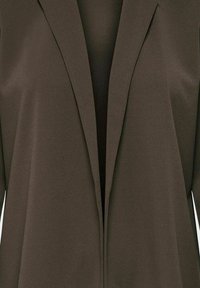 Blazer marrone con un tessuto liscio e texture. Presenta un colletto a scialle e un design aperto, mettendo in risalto il suo stile minimalista.