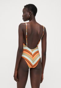 One-piece swimsuit featuring horizontal chevron stripes in orange, light blue, and brown. Open back and thin adjustable straps.