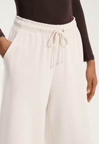 Krém színű, bő szárú nadrág, gumis derékkal és húzózsinórral. Oldalsó zsebekkel rendelkezik, sima, puha anyagú textúrával.