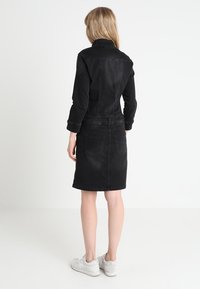 Svart denimklänning med långa ärmar, figurnära överdel och utsvängd kjol. Har två bakfickor och en naturlig midja.