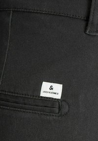 Pantalones negros con un bolsillo frontal que lleva una etiqueta blanca con la marca "JACK & JONES". La tela tiene una textura suave.
