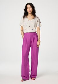 Grijze V-hals t-shirt met kleurrijke stippen; losse, hooggeprijsde fuchsia broek; platte sandalen met meerkleurige banden.
