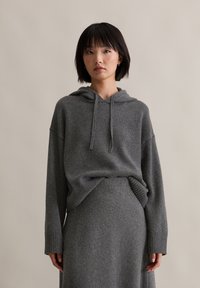 Grau gestrickter Hoodie mit lockerer Passform, Kordelzug am Hals und gerippten Bündchen, kombiniert mit einem passenden grauen Strickrock, der eine glatte Textur aufweist.
