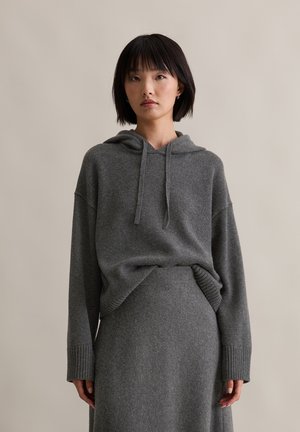 Grau gestrickter Hoodie mit lockerer Passform, Kordelzug am Hals und gerippten Bündchen, kombiniert mit einem passenden grauen Strickrock, der eine glatte Textur aufweist.