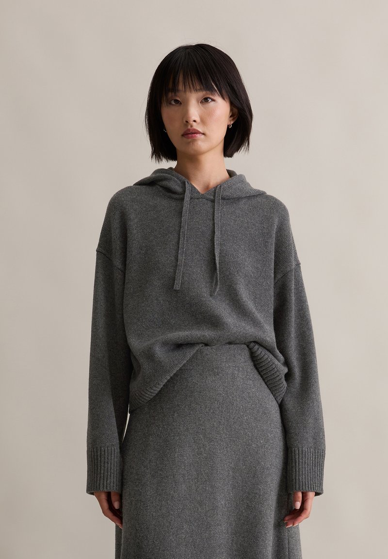 Grau gestrickter Hoodie mit lockerer Passform, Kordelzug am Hals und gerippten Bündchen, kombiniert mit einem passenden grauen Strickrock, der eine glatte Textur aufweist.