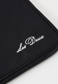 Sort stof laptop sleeve med en glat overflade, der har et hvidt broderet "Les Deux" logo og forstærkede sømme.