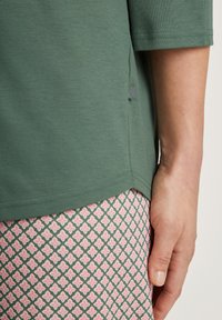 Camicia di cotone verde con maniche a tre quarti, dotata di uno spacco laterale. Abbinata a un tessuto a fantasia rosa e verde, caratterizzato da un motivo a diamante.