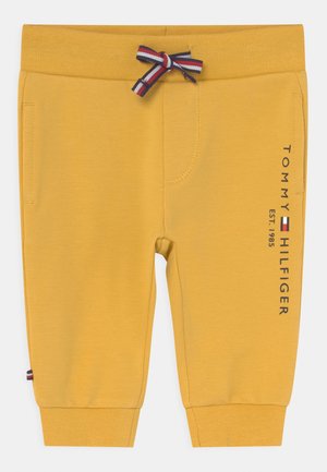 Pantalones deportivos amarillos para niños pequeños con puños acanalados, un lazo de cordón a rayas, bolsillos laterales y la marca Tommy Hilfiger en vertical en la pierna.