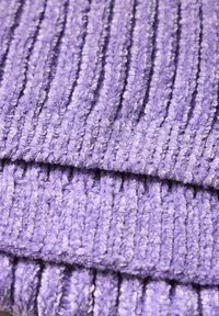 Tissu violet côtelé avec une texture moelleuse, présentant des lignes verticales et un aspect doux et duveteux. Mise au point sur les détails tactiles et de couleur.