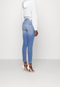 Obcisłe jeansy w jasnoniebieskim denimu z efektem wypłowienia, tylnymi kieszeniami i paskiem z logo, zestawione z białą krótką bluzą z kapturem i beżowymi szpilkami.