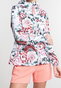 Chaqueta de flores con cremallera y fondo blanco, con flores rosas y rojas, capucha y bolsillos funcionales; combinada con pantalones cortos color coral.