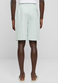 Ljus mintgröna shorts med elastisk midja och ett bakfick. Materialet verkar mjukt och något texturerat. Avslappnad design.