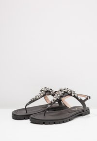 Svarta platta sandaler med en texturerad gummisula, med en dekorativ rem prydd med klara rhinstenar och en minimalistisk design.