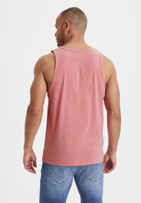 Red heathered tank top with a round neckline and wide shoulder straps, paired with medium-wash blue jeans. Casual fit, minimal detailing.