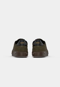 Mørkegrønne semskede sneakers med sorte accenter ved hælen, med et teksturert design og merkevarenavnet "BOSS" i gull bak.