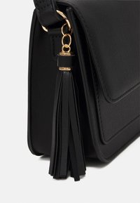 Borsa nera in ecopelle con pattina, caratterizzata da un dettaglio a frangia in metallo dorato sul lato e una finitura texturizzata. Forma rettangolare.