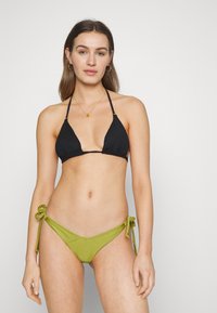 Top de bikini triangular preto com textura canelada; parte de baixo de natação verde-azeitona com laterais com laço. Tecido suave, design minimalista, esquema de cores em duas tonalidades.