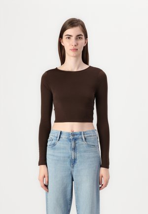 Brown, long-sleeve crop top in a smooth fabric, paired with light blue high-waisted jeans featuring a button front and straight-leg design.