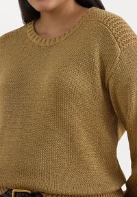 Knit pulóver arany árnyalatban, kerek nyakkivágással, textúrált vállbetéttel és laza fazonnal, sima, fényes fonallal.