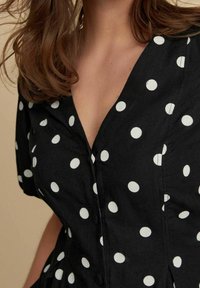 Abito nero con pois bianchi, caratterizzato da una scollatura a V, maniche corte e dettagli con bottoni lungo il davanti e in vita.