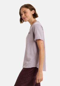 Licht paarse T-shirt met korte mouwen en een ronde hals, met een klein hartlogo in bordeauxrood aan de linkerkant, gemaakt van zachte materialen.