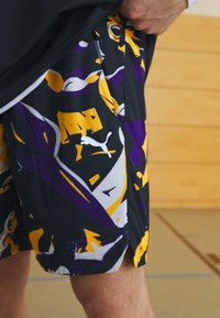 Pantalones cortos deportivos con una base negra y patrones abstractos salvajes en púrpura y amarillo. Incluye un logo blanco de Puma en la tela.