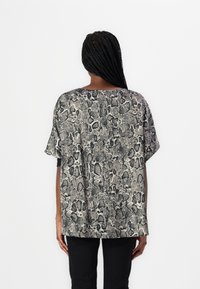 Djurtryck, kortärmad blus i nyanser av beige och svart, med en löst sittande passform och mjuk textur, kombinerad med svarta byxor.