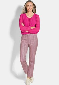 Roze blouse met een aangesloten halslijn, gecombineerd met strakke, gepatternde broeken in roze en wit, afgemaakt met lichte sneakers.