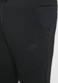Närbild av svarta Nike-sweatpants som visar sidofickan, dragsnöret och den diskreta Nike-logotypen på låret.