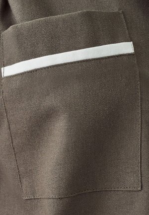 Brunt stof med en tekstureret overflade har en rektangulær lomme, der har en hvid vandret stribe over den øverste kant.