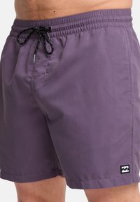 Μωβ μαγιό με ελαστική μέση, κλείσιμο με κορδόνι και μικρό μαύρο και άσπρο λογότυπο στο αριστερό πόδι. Απαλή υφή.