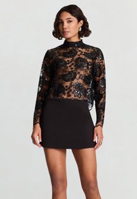 Top en dentelle noire avec broderie florale, manches longues, col montant, assorti à une mini jupe noire. Texture transparente avec détails d'ourlet festonné.