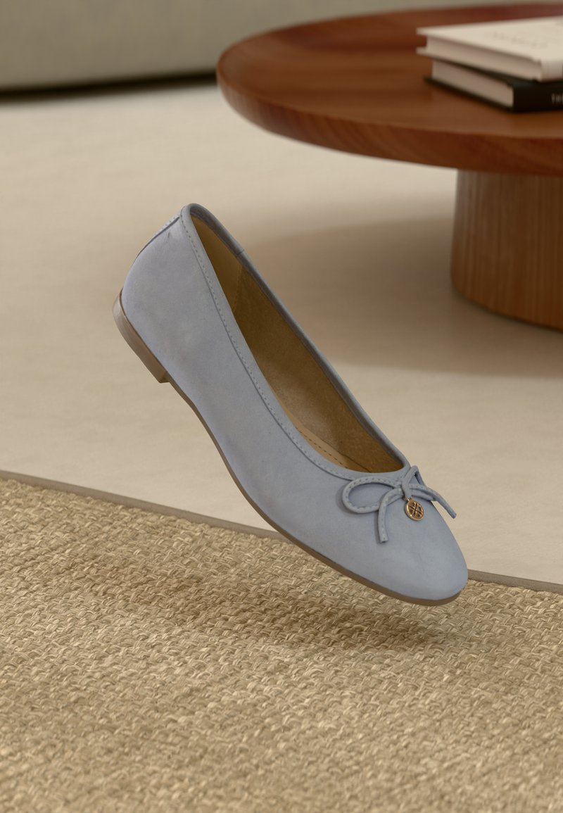 Ballerine en daim bleu clair avec un nœud décoratif et un petit logo, conçue avec un bout arrondi et une semelle plate basse.